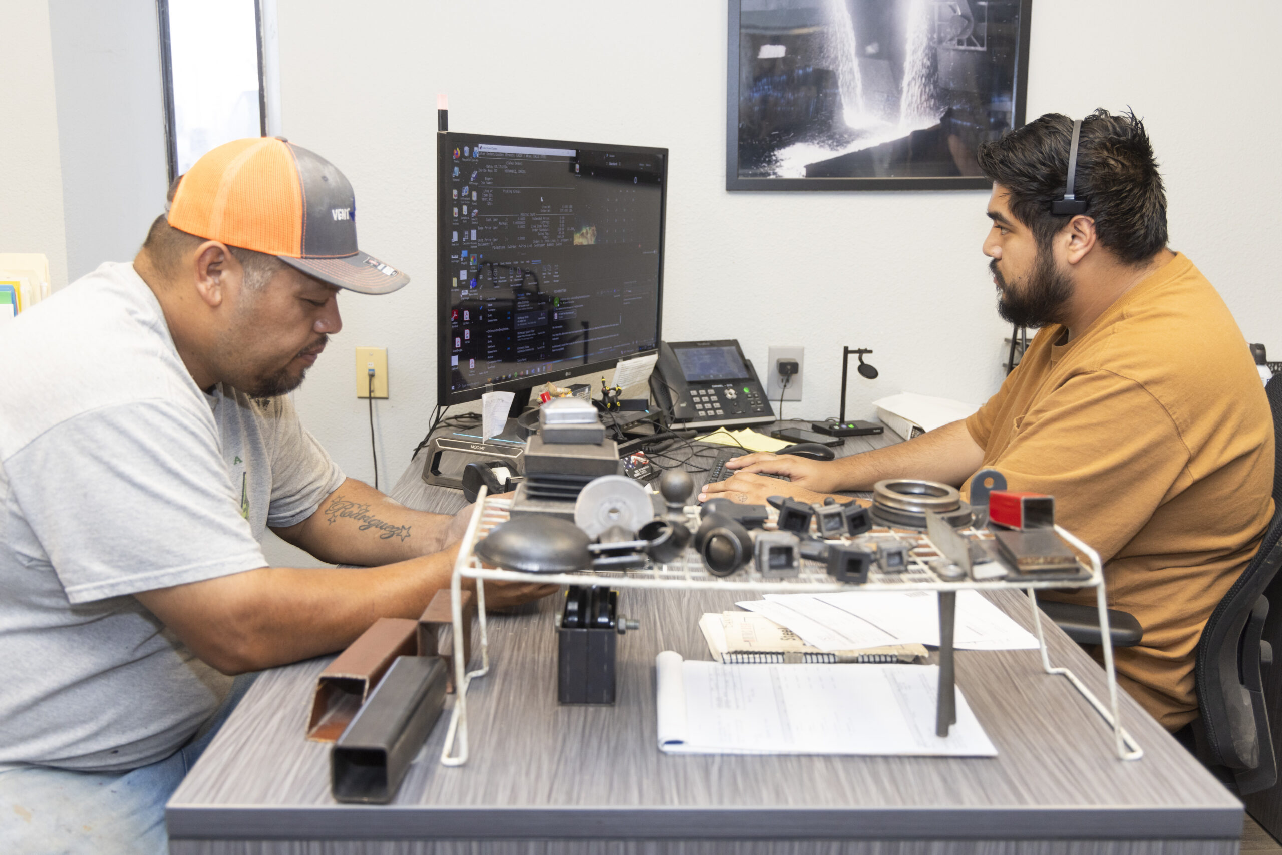 A man making a steel purchase from a man with a headset at a computer